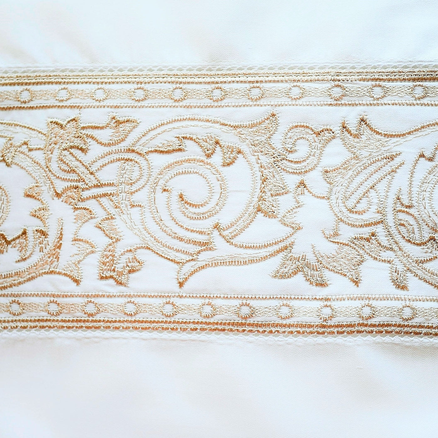 Close-up of gold embroidered baroque scroll border on ivory linen pillow sham.