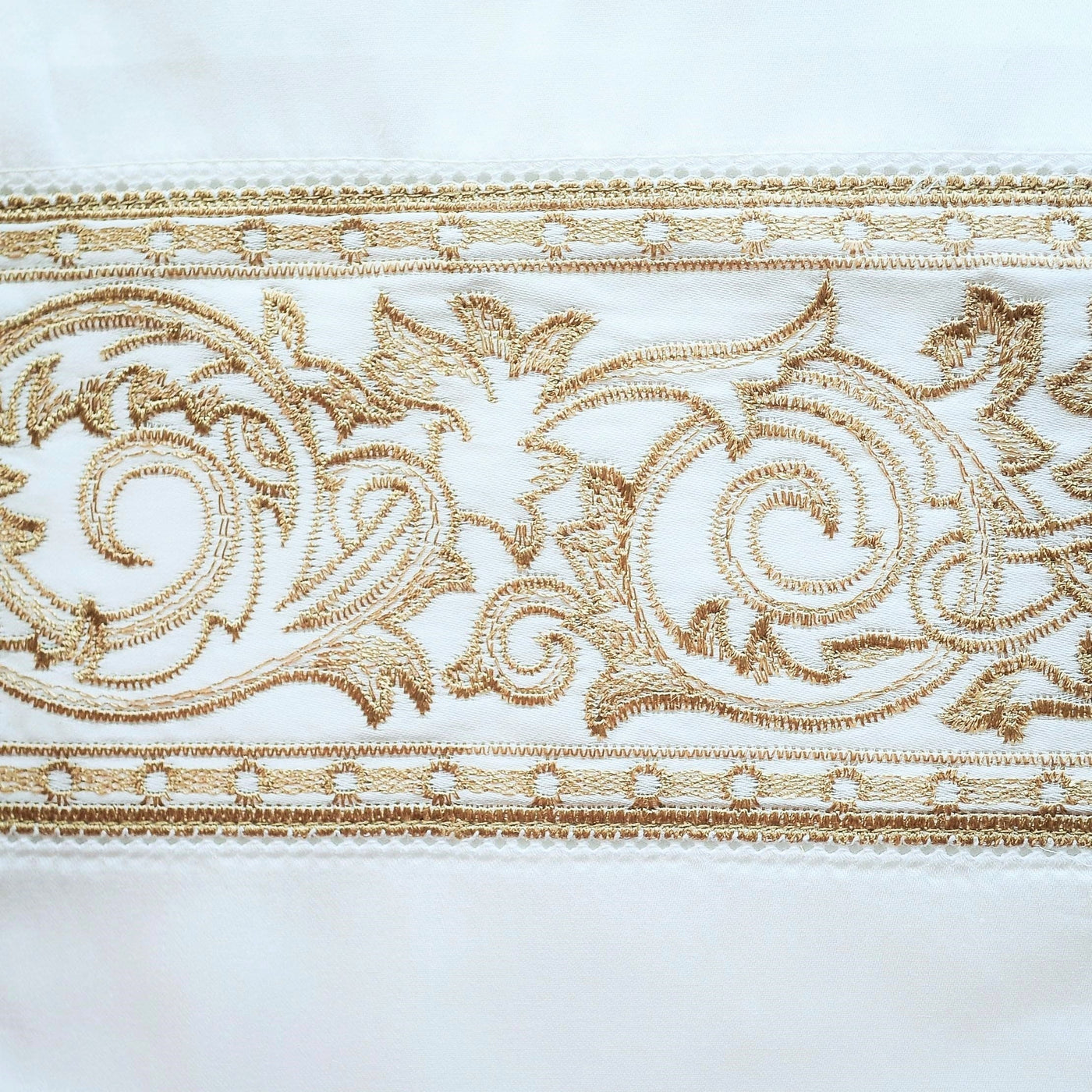 Close-up of gold embroidered acanthus scroll border on ivory cotton flat sheet.
