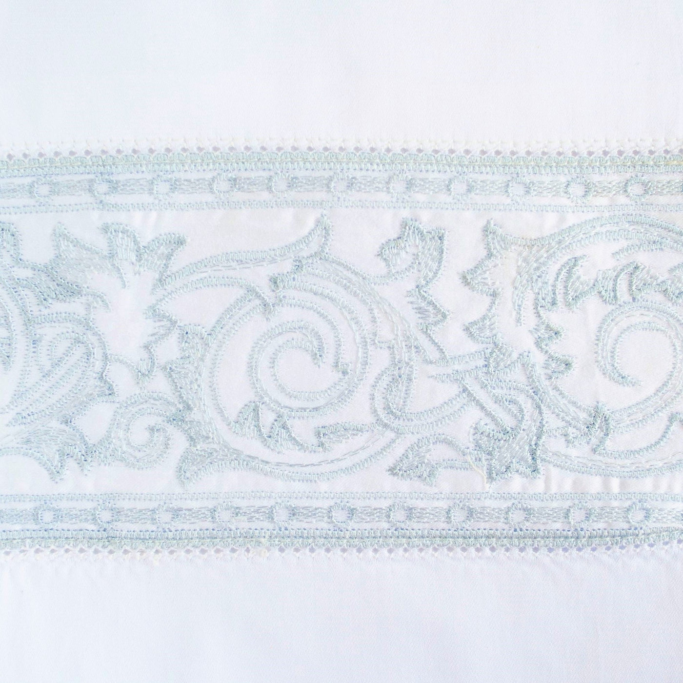 Close-up of aqua embroidered acanthus scroll trim on white flat sheet.