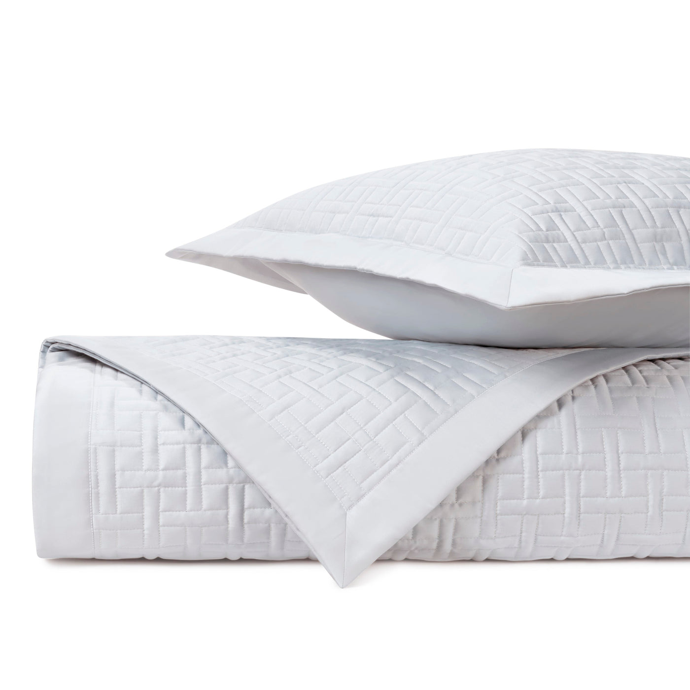 Close-up of white quilted parquet-pattern coverlet and sham, folded and stacked.