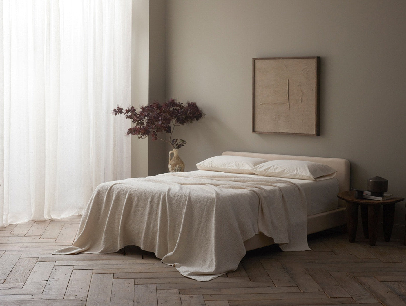 Ivory matelasse blanket draped over a made bed in a neutral, light-filled bedroom.