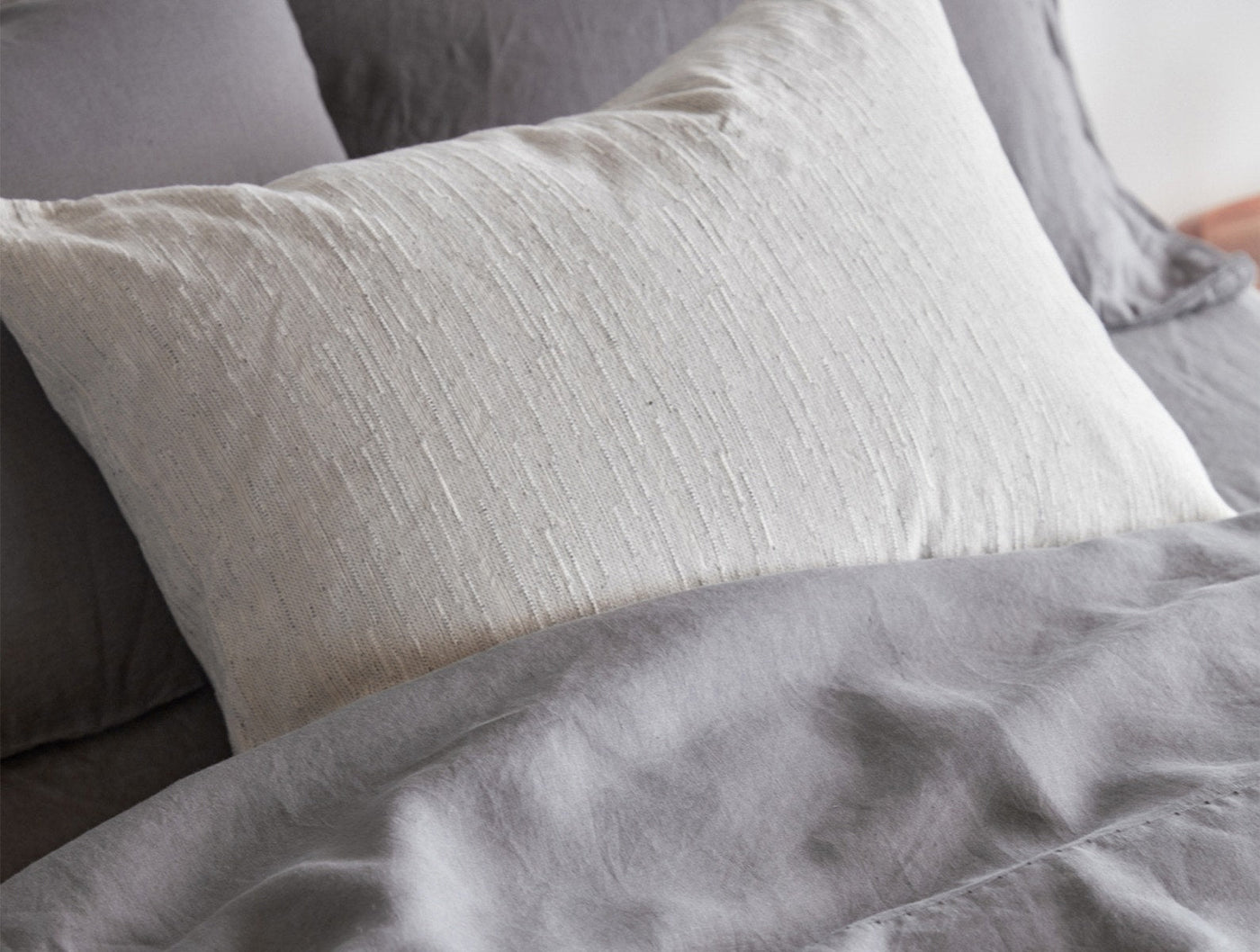 Close-up of ivory textured pillowcase against gray linen duvet, showing natural fabric weave detail.
