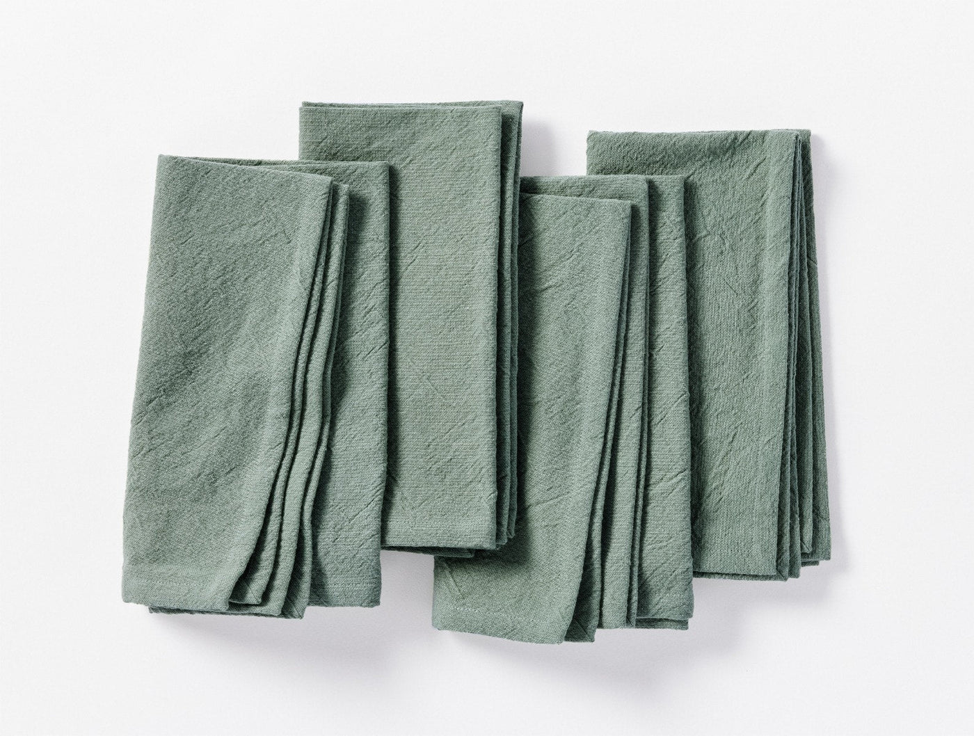 Overhead view of four sage green Coyuchi Sonoma Textured linen napkins folded and fanned.