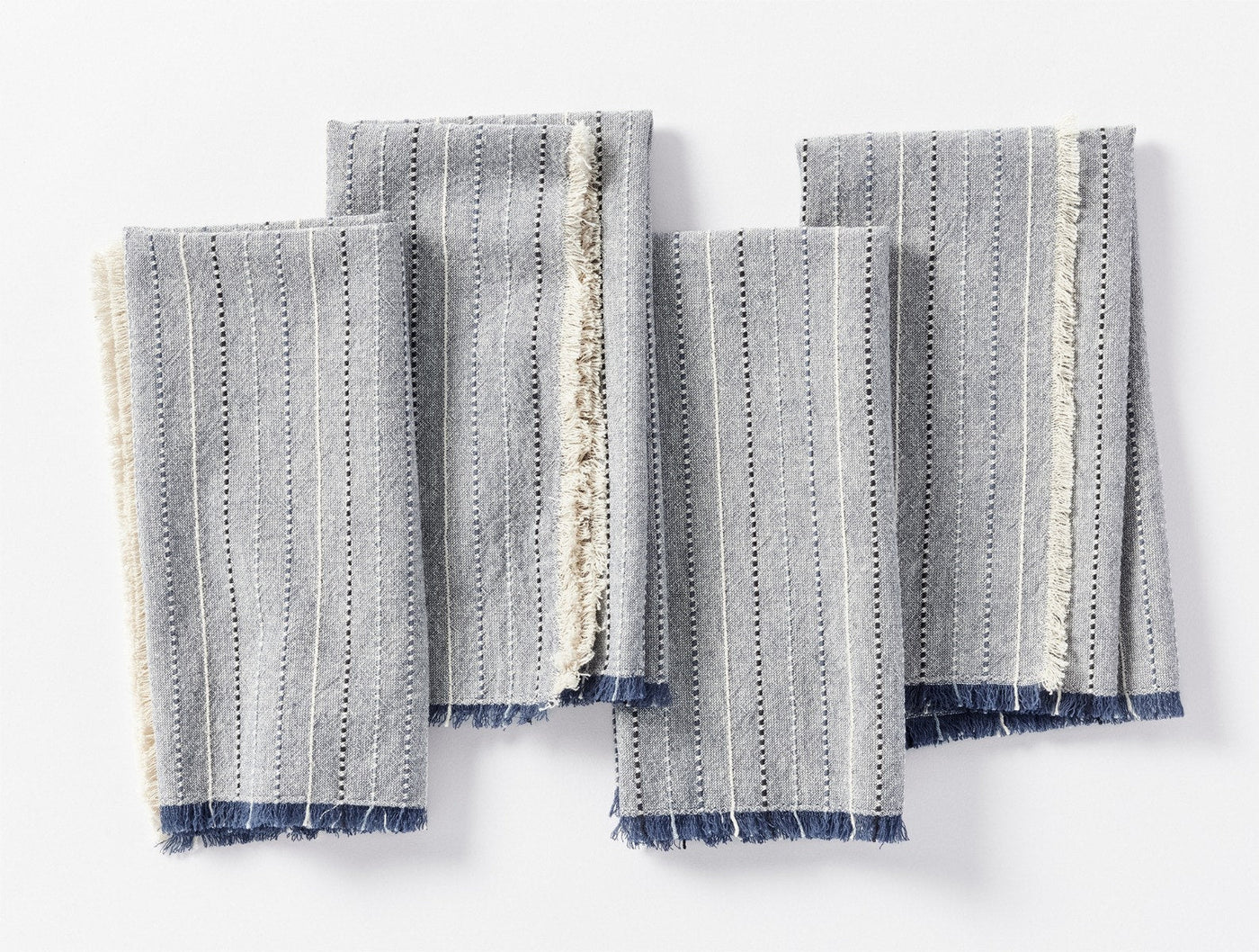 Coyuchi Fringe Stripe napkins fanned flat, showing frayed indigo and ivory fringe edges.