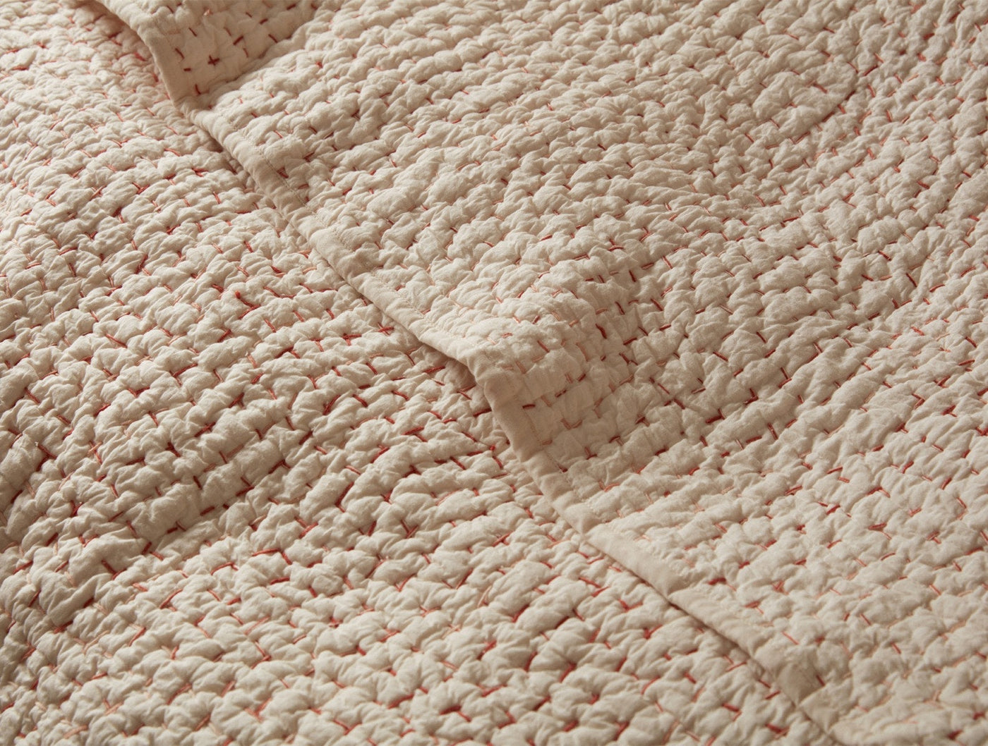 Close-up of Coyuchi Pebbled Handstitched quilt corner seam in blush with coral fleck texture.