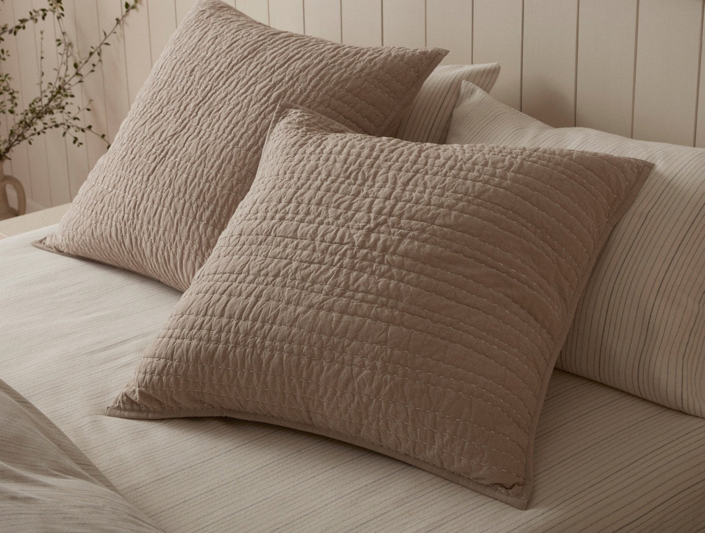 Close-up of Coyuchi Channel Handstitched shams in taupe, showing quilted texture on styled bed.
