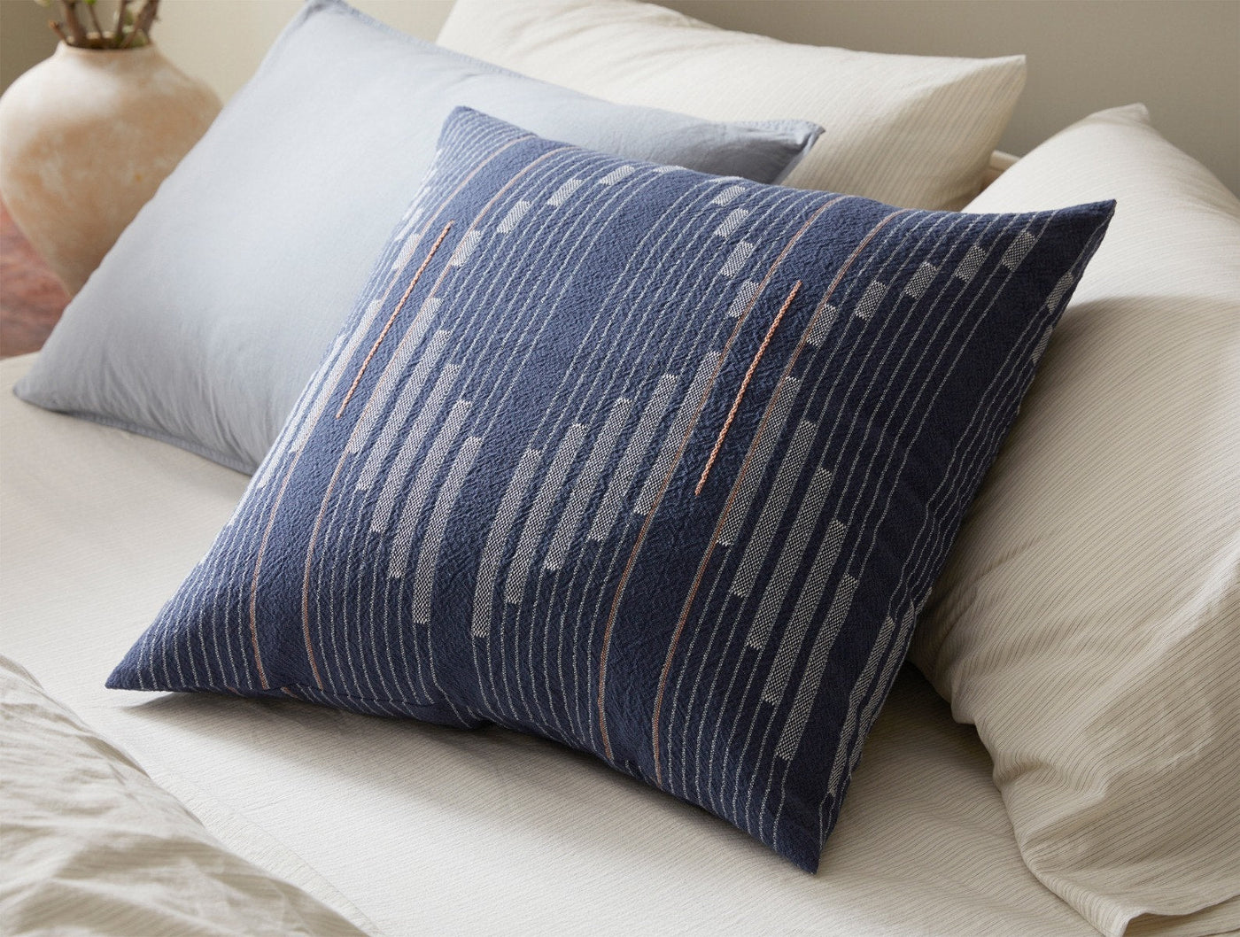 Coyuchi Morelia pillow styled on bed, navy blue woven stripe pattern, close view.