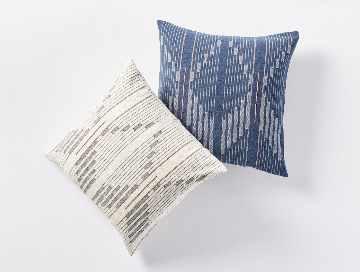Two Coyuchi Morelia pillows, ivory and slate blue, with geometric dash stripe pattern.