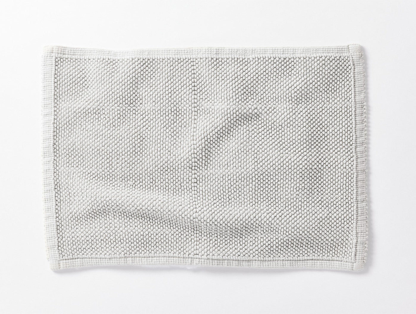 Coyuchi Pebbled bath rug in white, overhead view showing textured knit weave and fringe trim.