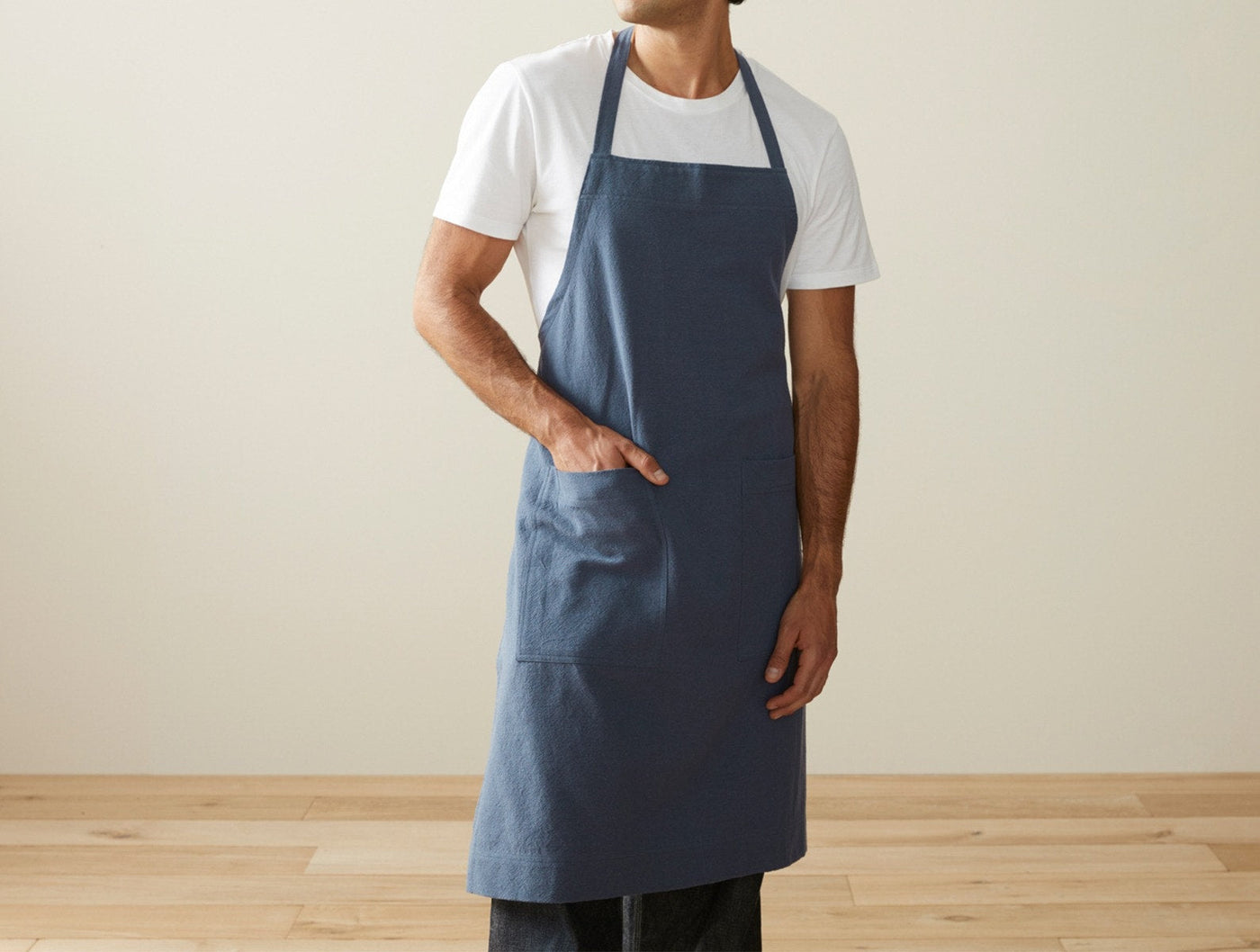 Coyuchi slate blue linen apron worn by a man, hand in front pocket.