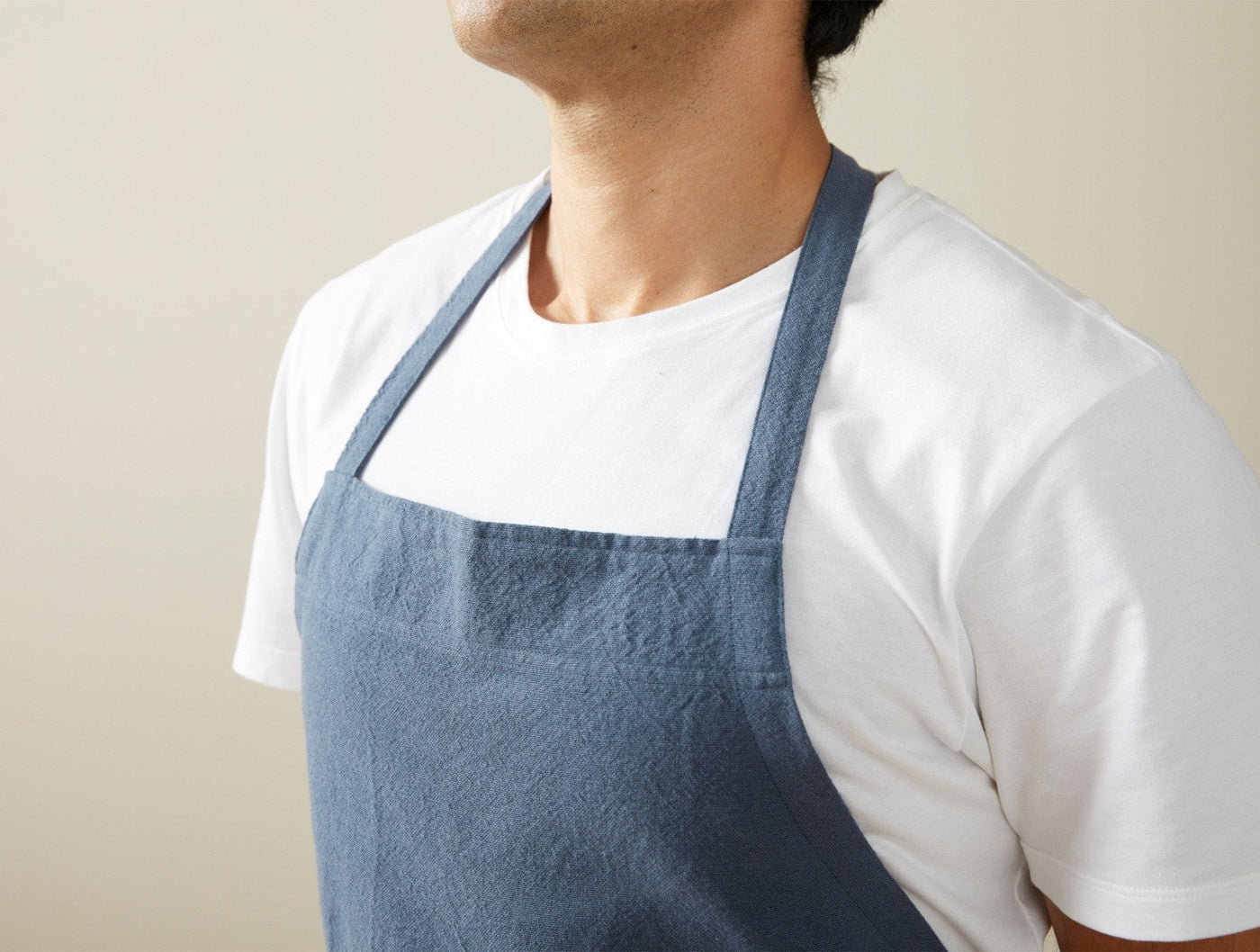 Close-up of Coyuchi Sonoma Textured apron in slate blue worn over white tee, showing neck strap and bib.