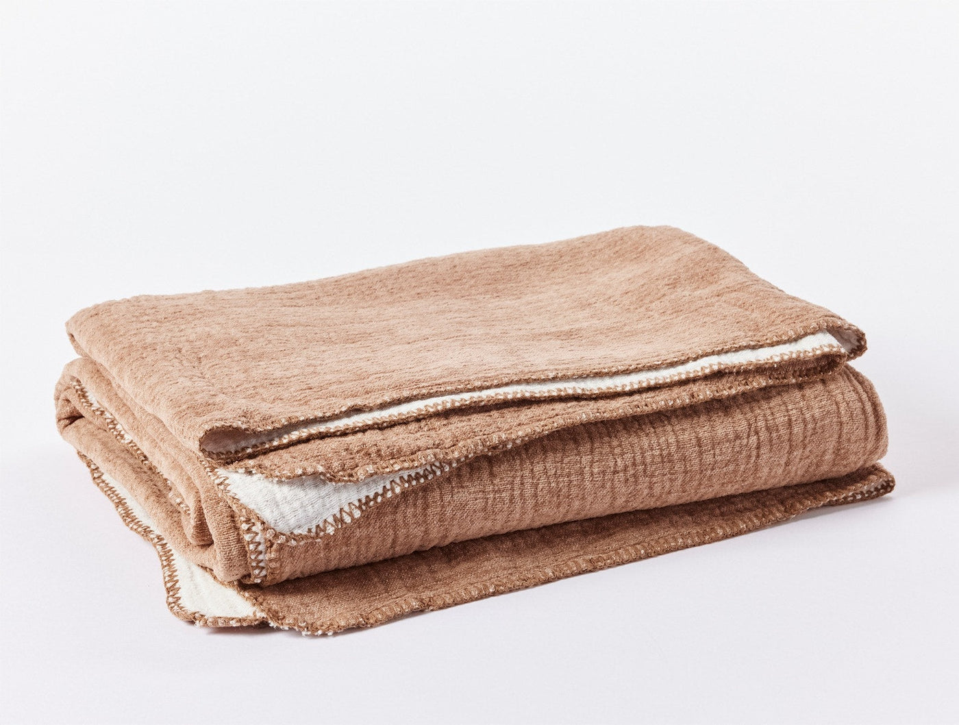 Folded camel and ivory reversible cotton blanket showing contrast lining at edges.