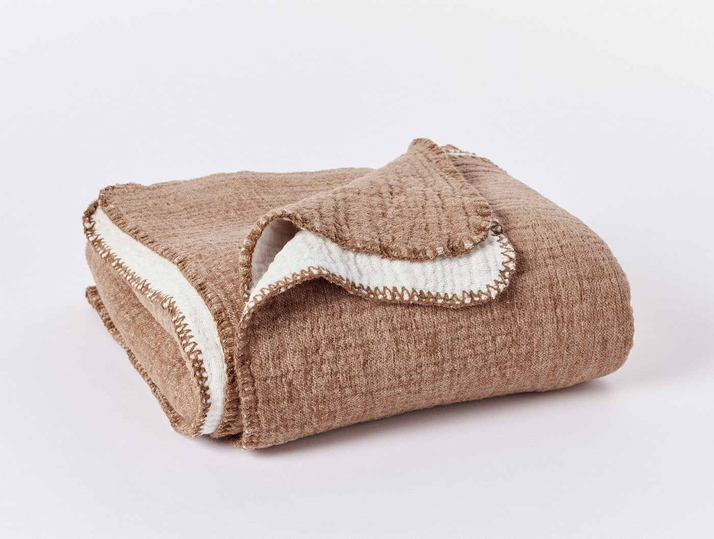 Folded camel and ivory Coyuchi Cozy Cotton Throw showing blanket stitch trim detail.