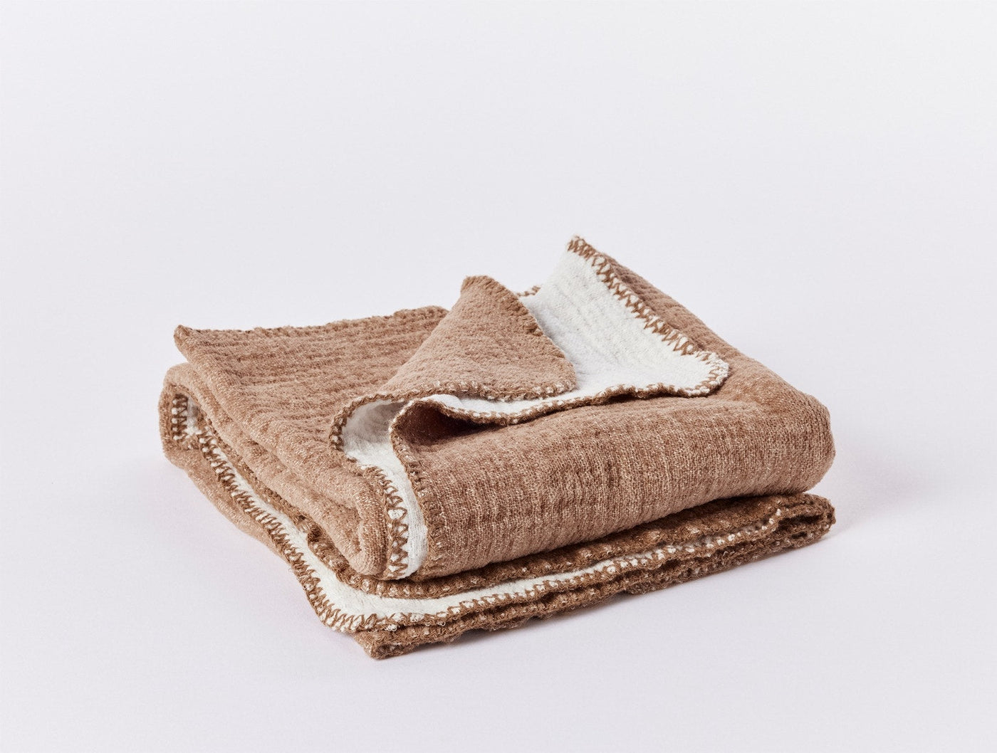 Folded camel and ivory reversible cotton blanket showing contrast whipstitch trim detail.