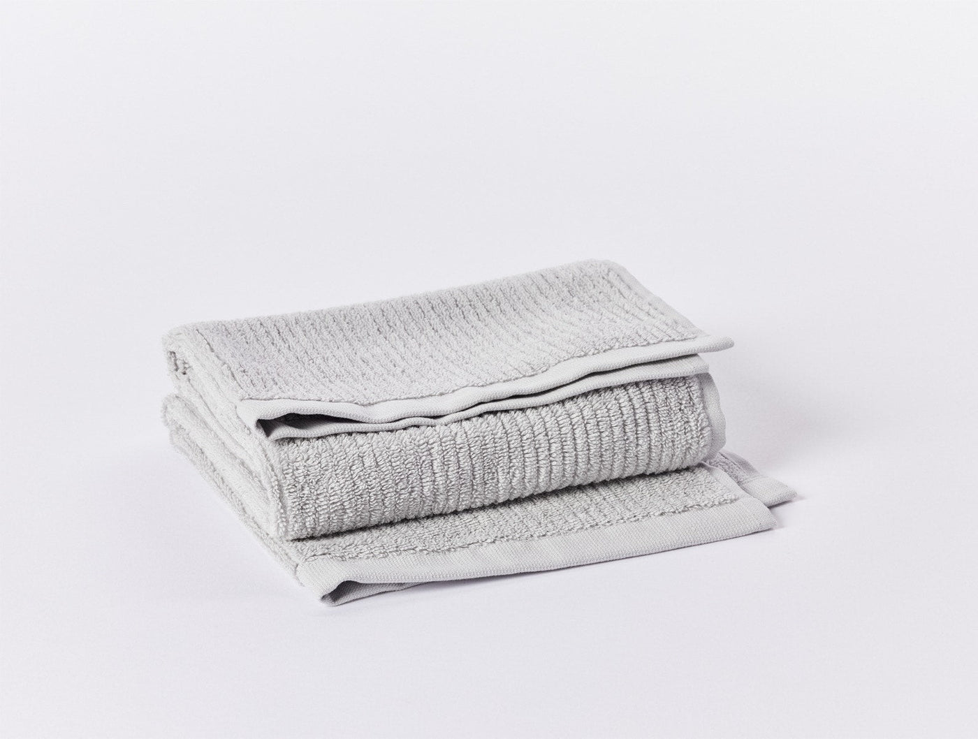Folded silver grey ribbed terry bath towels stacked, showing textured weave and smooth border hem.