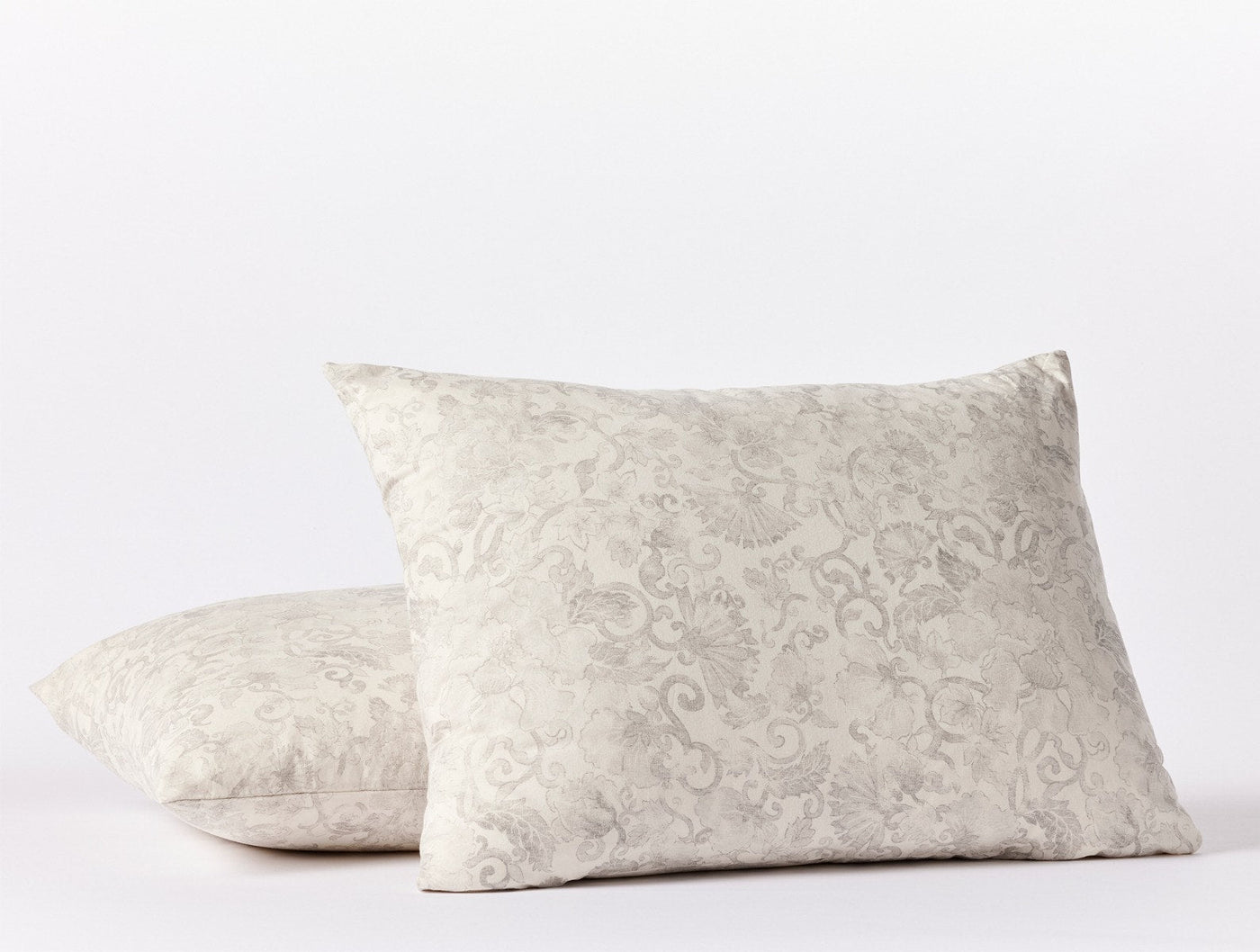 Ivory damask-print pillow shams stacked, showing ornate floral scrollwork pattern.