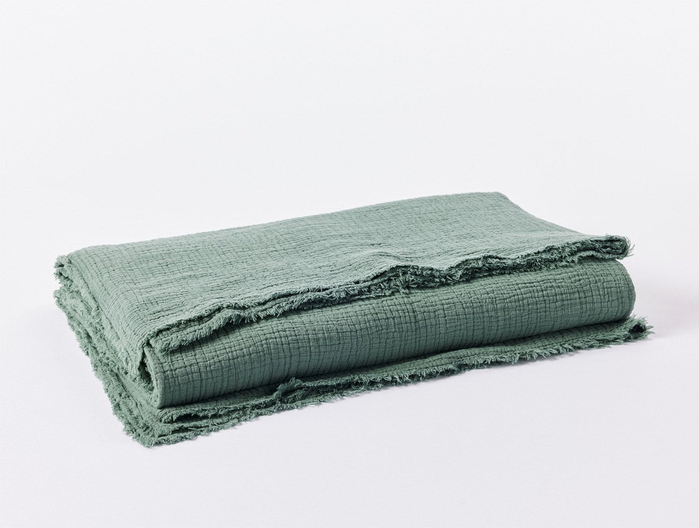 Close-up of sage green matelasse blanket folded, showing frayed edge trim detail.
