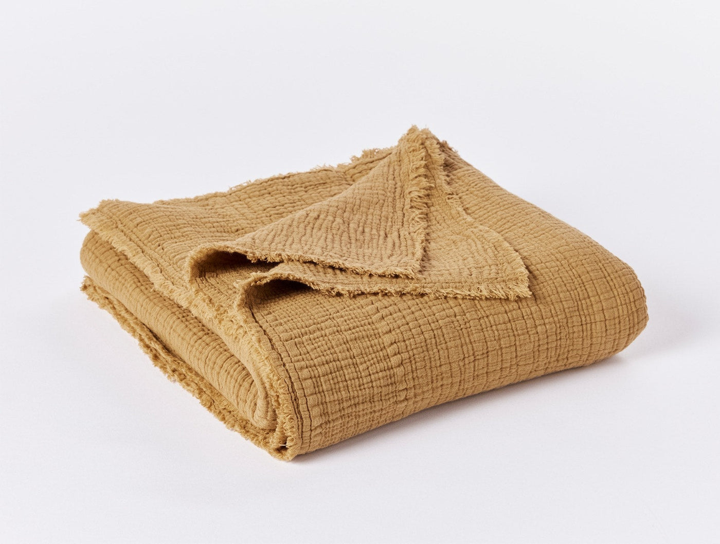Folded mustard cotton matelassé throw with frayed edges, showing textured weave detail.