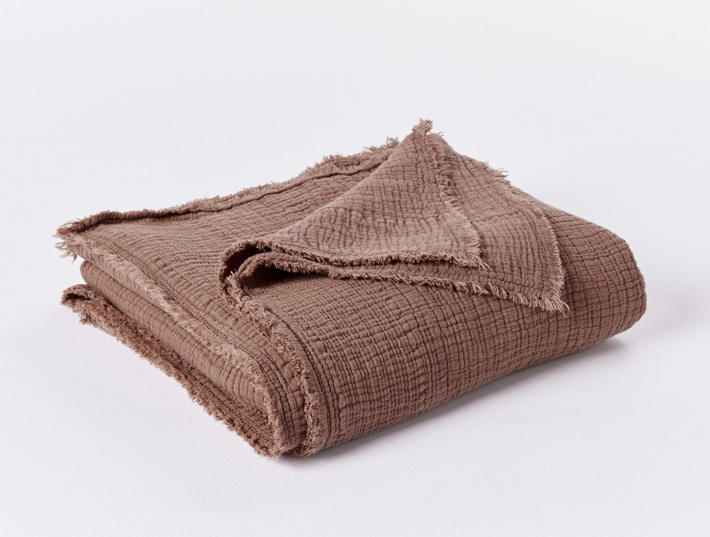 Frayed edge detail on folded Topanga Matelasse throw in warm mauve-brown matelasse weave.