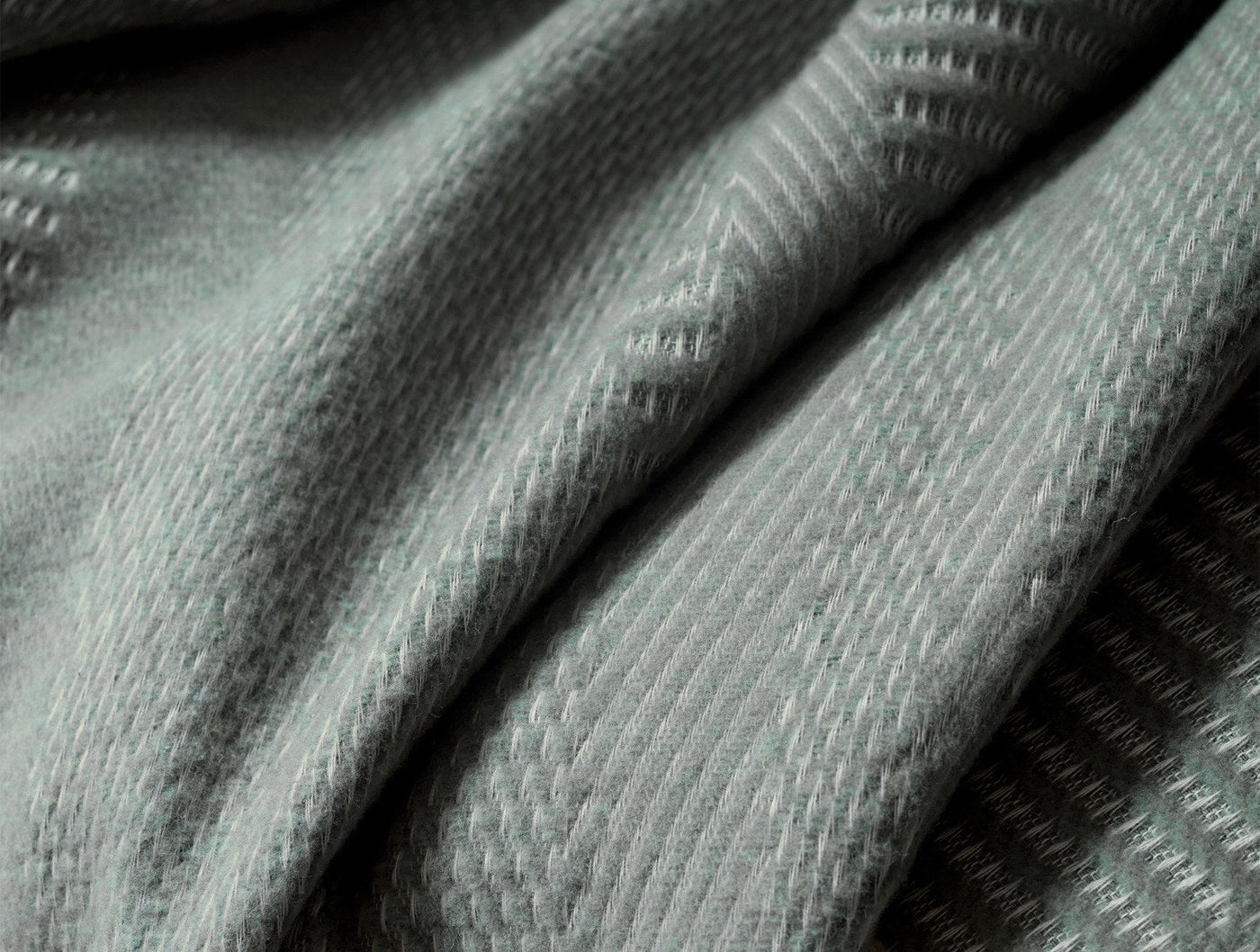 Close-up of sage green woven throw fabric with textured diamond pattern and soft drape.
