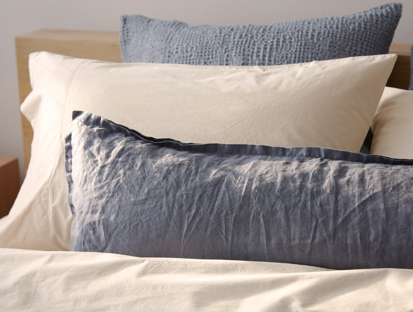 Slate blue relaxed linen pillow shams layered over ivory bedding on a styled bed.