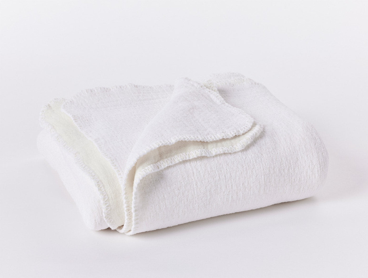 Folded ivory cotton blanket showing textured weave and scalloped trim detail.