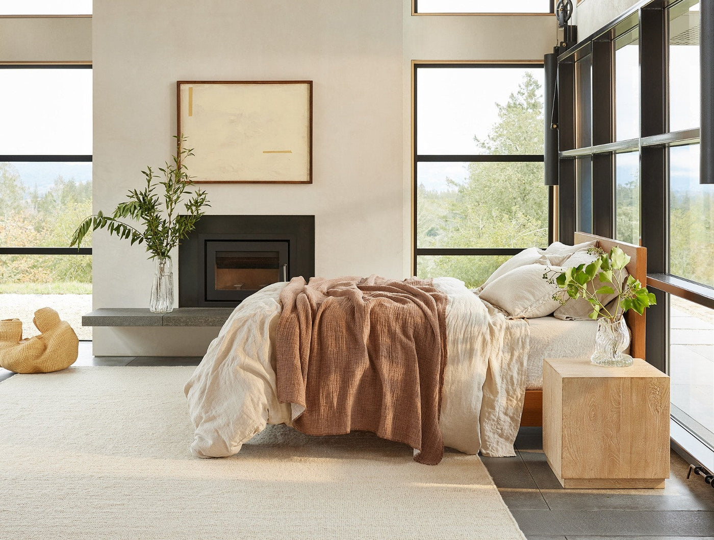 Coyuchi Cozy Cotton blanket in terracotta draped over bed in modern room with fireplace.
