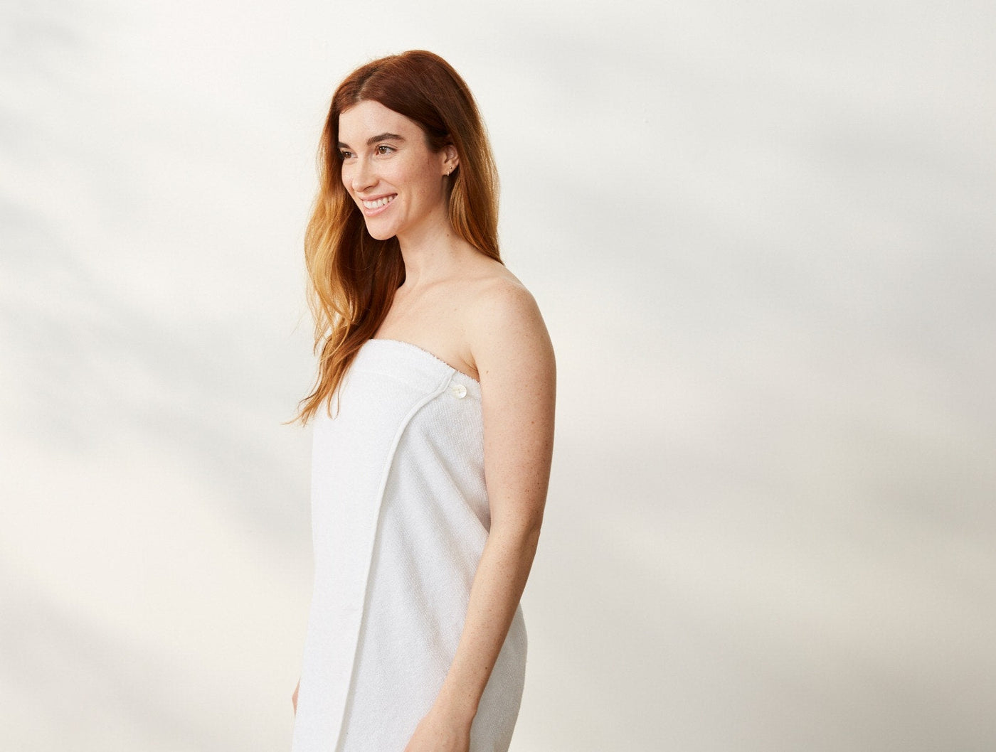Woman wrapped in Coyuchi Air Weight white bath wrap, side profile view.