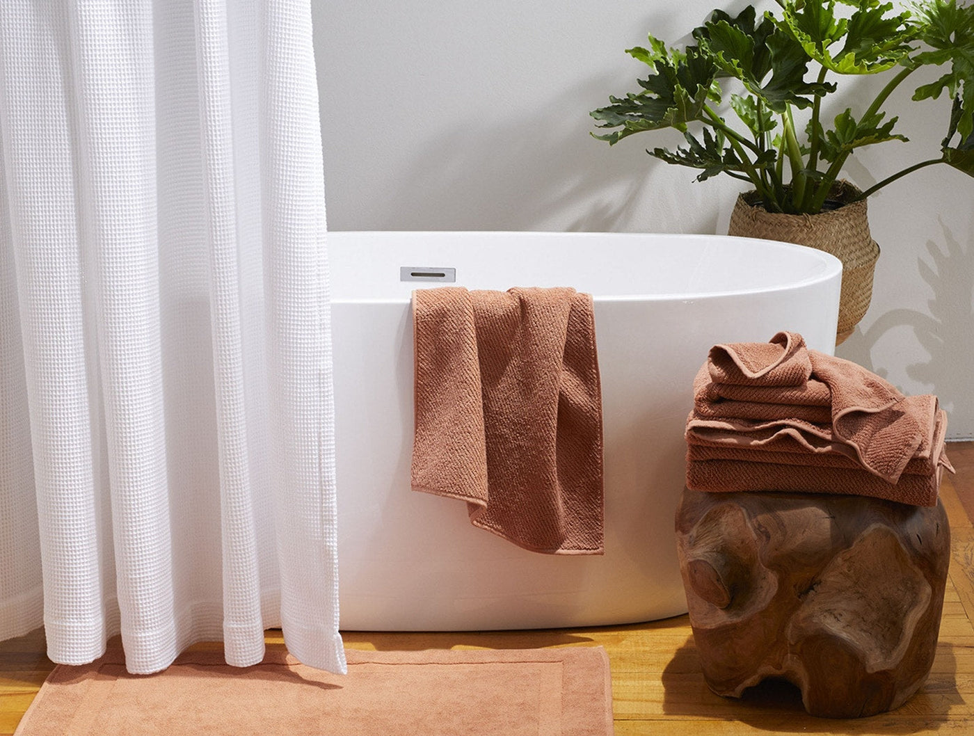 White Coyuchi waffle shower curtain beside a freestanding tub, styled with terracotta towels.
