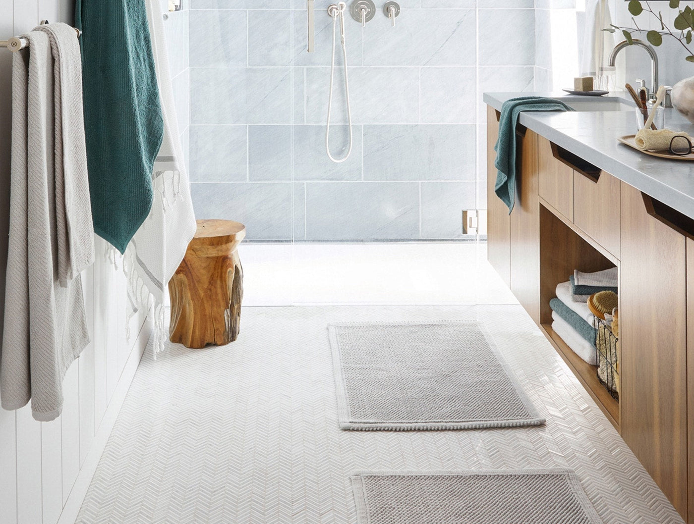 Coyuchi Pebbled bath rugs in silver styled on white bathroom floor with teal towels.