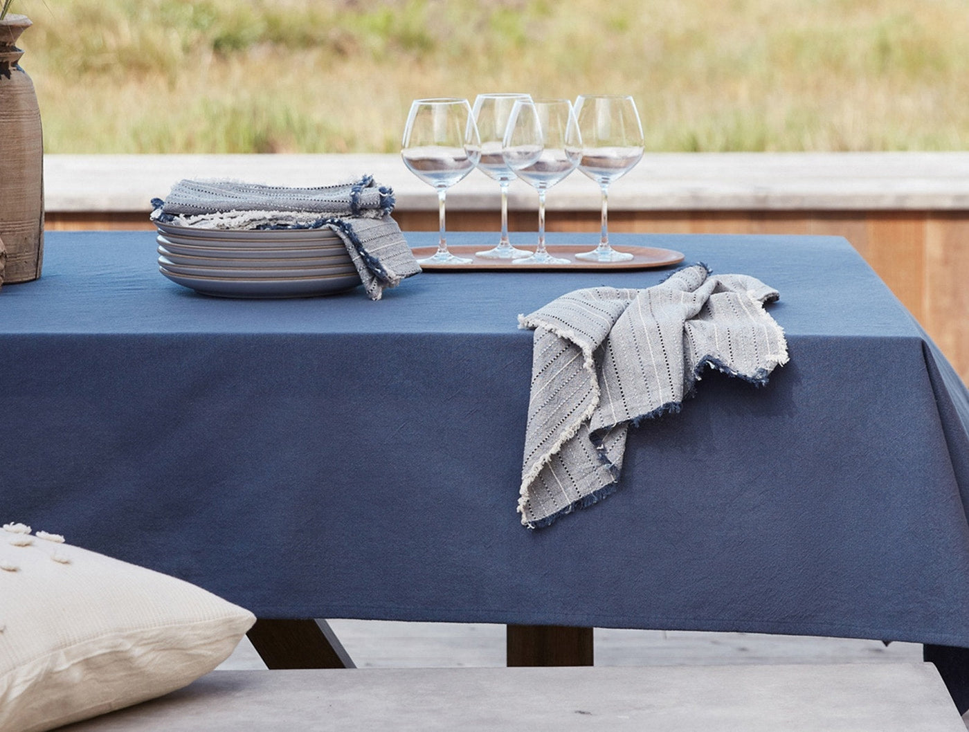 Fringe stripe napkins in natural tones draped on a navy linen tablecloth, outdoor setting.