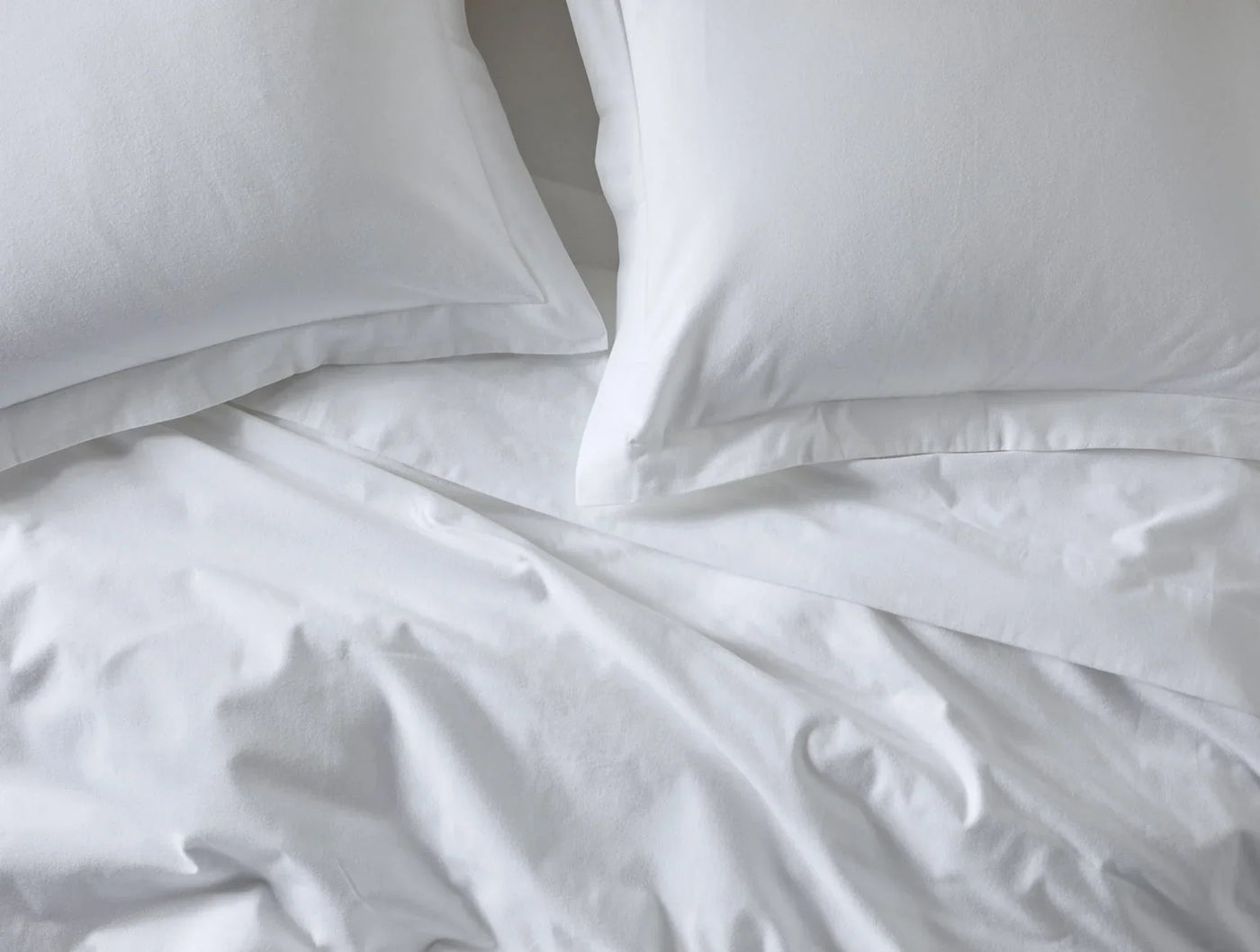 Coyuchi Cloud Brushed Flannel pillow shams in white on a softly rumpled bed.