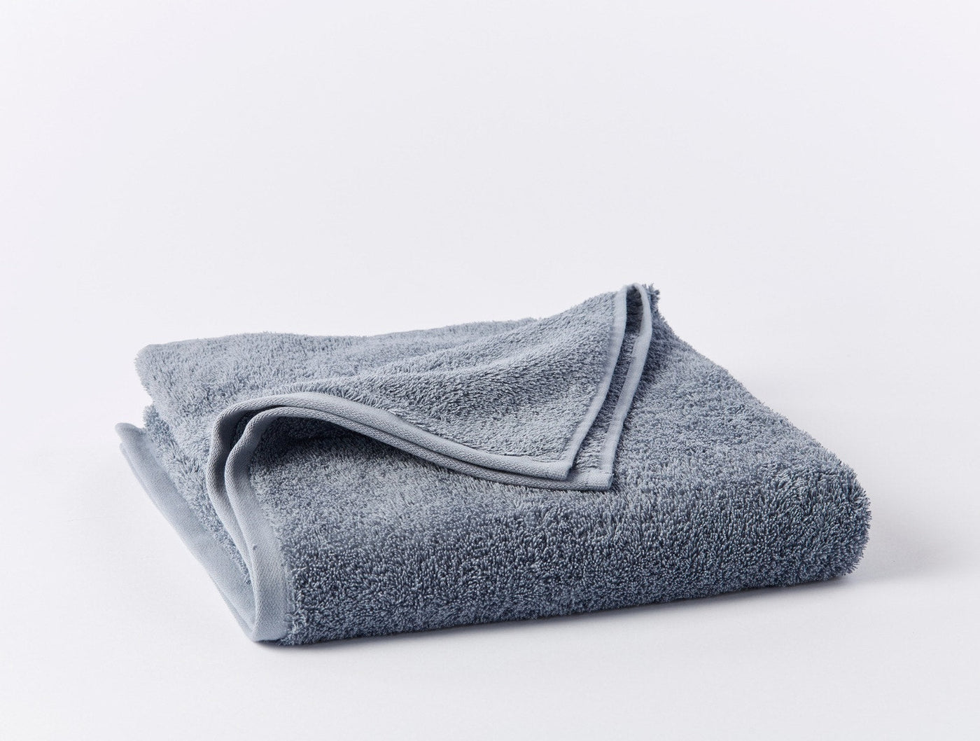 Folded slate blue Coyuchi Cloud Loom bath towel showing plush terry texture and finished edges.