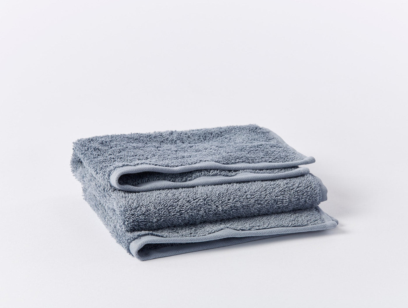 Two slate blue Coyuchi Cloud Loom bath towels folded and stacked on white background.
