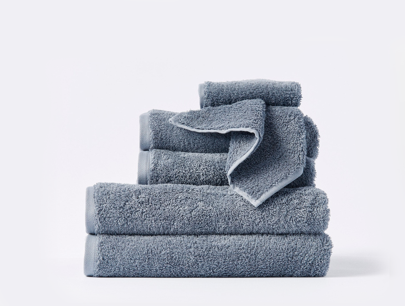 Close-up of stacked Coyuchi Cloud Loom towels in slate blue, showing varied sizes with plush pile texture.