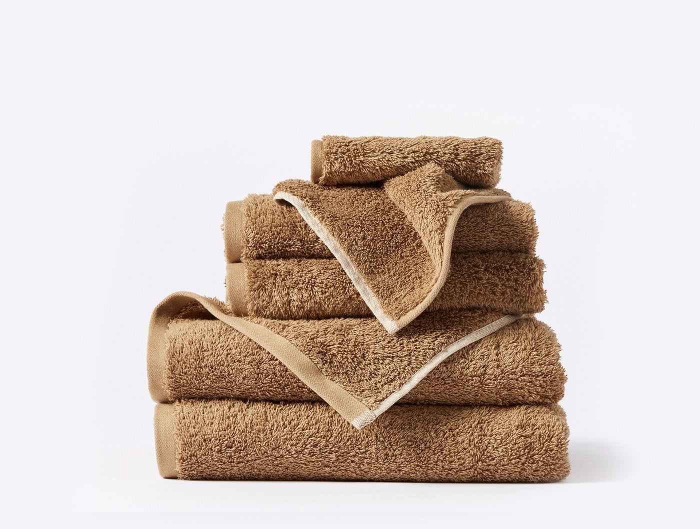 Stacked camel Coyuchi Cloud Loom towel set showing varied sizes with ivory trim detail.
