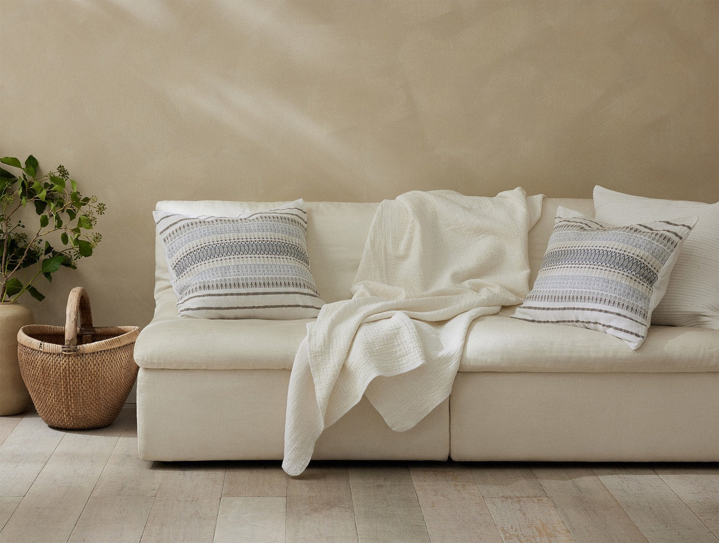 Coyuchi Cozy Cotton Throw in ivory draped over a cream sofa with striped accent pillows.
