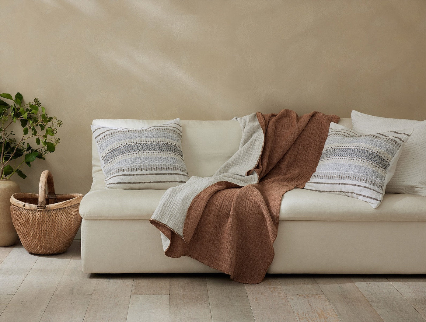 Terracotta quilted throw draped over a cream sofa, styled with striped cushions.