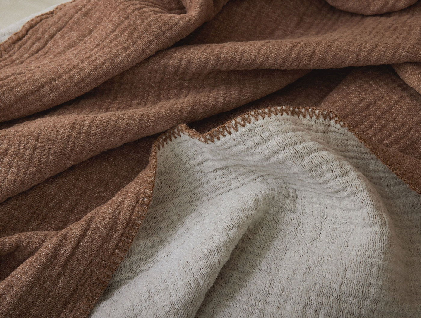 Close-up of Coyuchi Cozy Cotton blanket reverse, showing toffee and ivory textured weave with blanket-stitched edge.