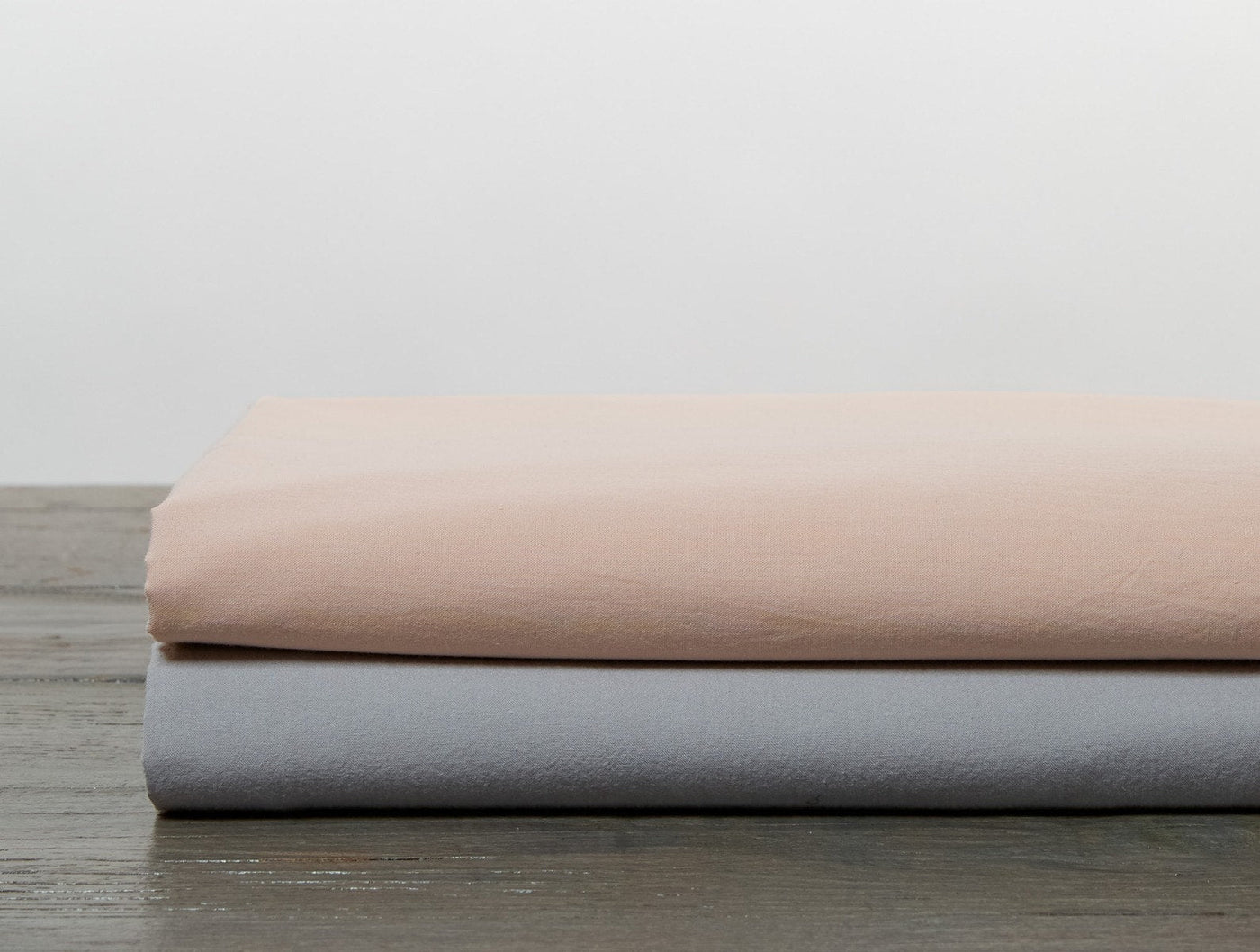 Blush and gray fitted sheets folded and stacked on a dark wood surface.