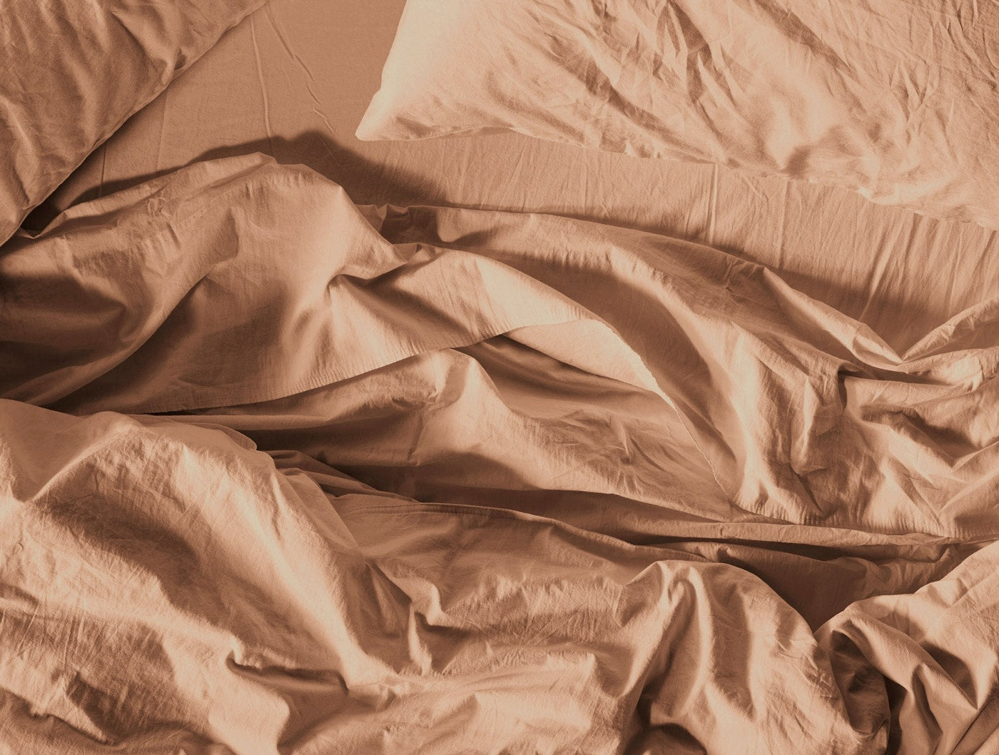 Coyuchi Crinkled Percale pillowcase in terracotta, casually rumpled on a bed.