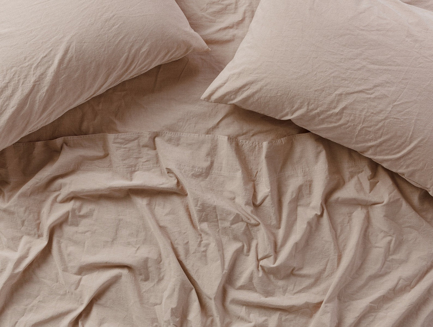 Blush crinkled percale fitted sheet with matching pillowcases, overhead view showing relaxed texture.