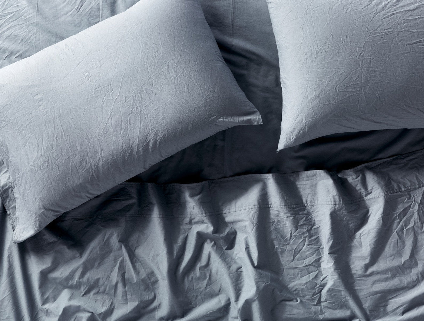 Overhead view of rumpled slate blue Coyuchi Crinkled Percale pillowcases against darker duvet.