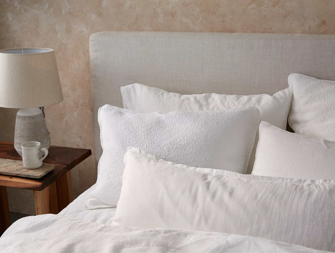 Coyuchi Relaxed Linen pillow styled on a made bed with layered white bedding.