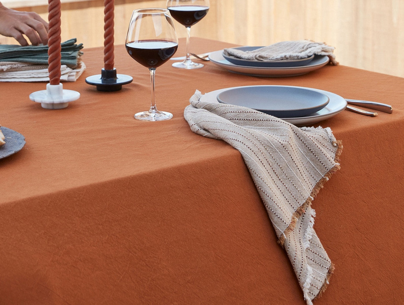 Ivory striped linen napkin with fringe trim on terracotta tablecloth, styled with slate blue plates.