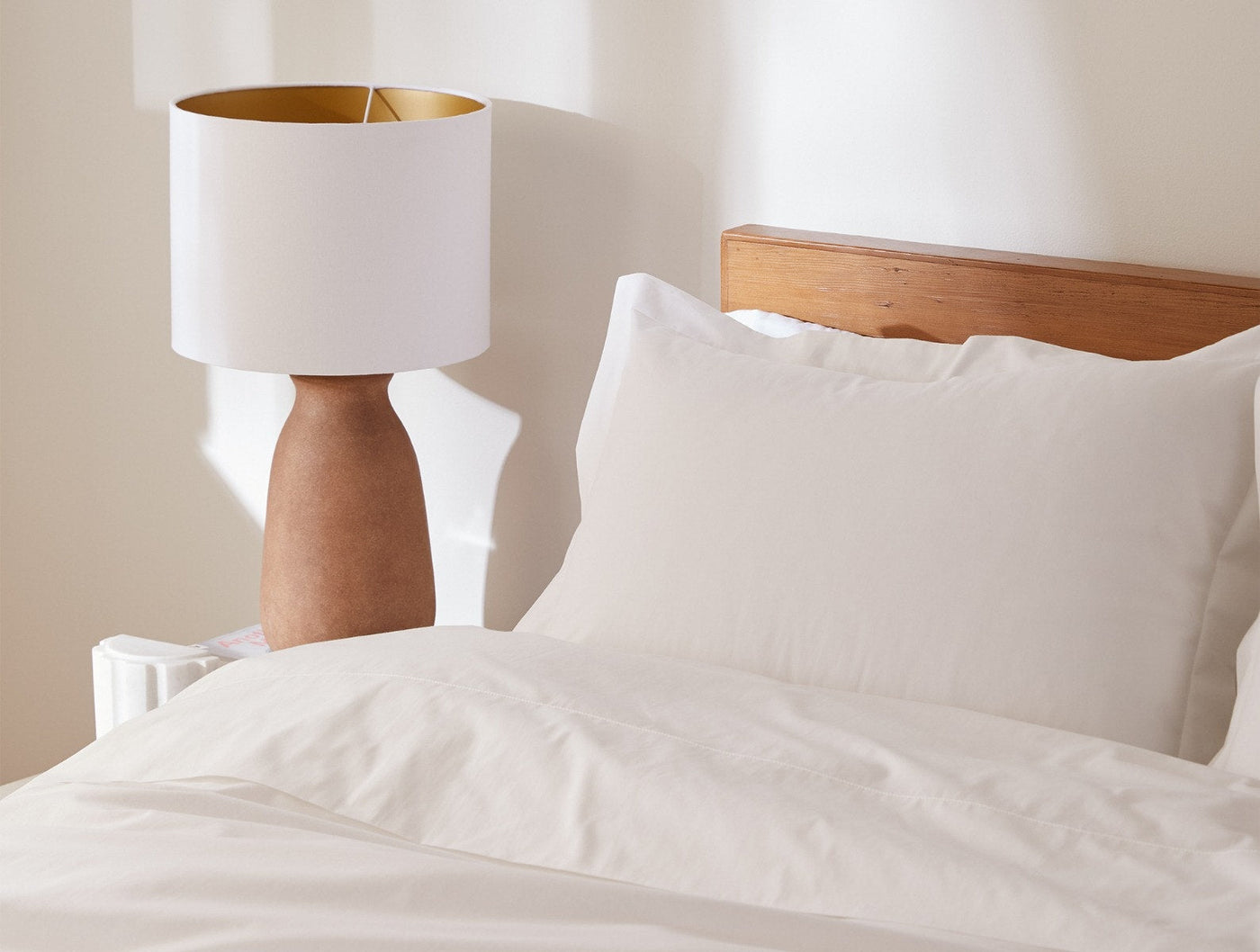 Coyuchi Heritage Percale pillowcases in white styled on bed beside warm wood lamp.
