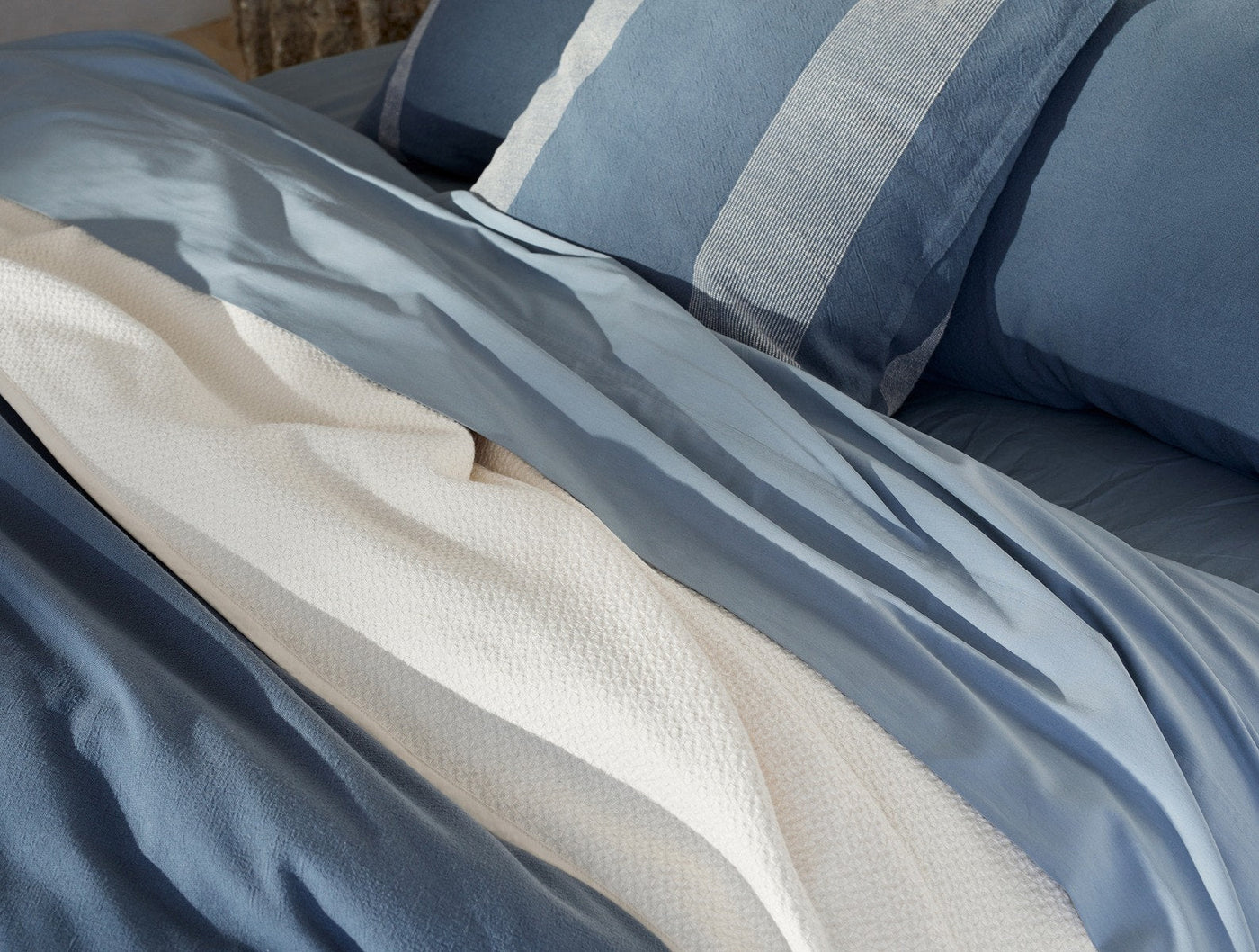 Close-up of ivory honeycomb-textured blanket draped over blue linen bedding.