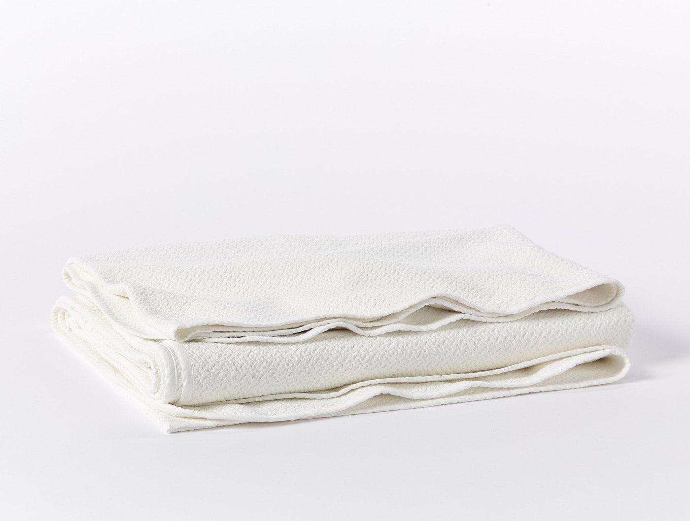 Coyuchi Honeycomb blanket folded, showing ivory textured weave and hemmed edges.