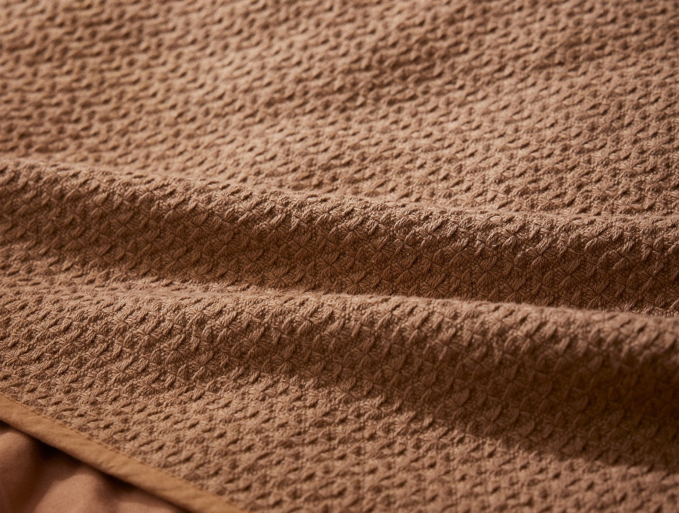 Close-up of Coyuchi Honeycomb blanket in caramel, showing textured weave with soft draping.