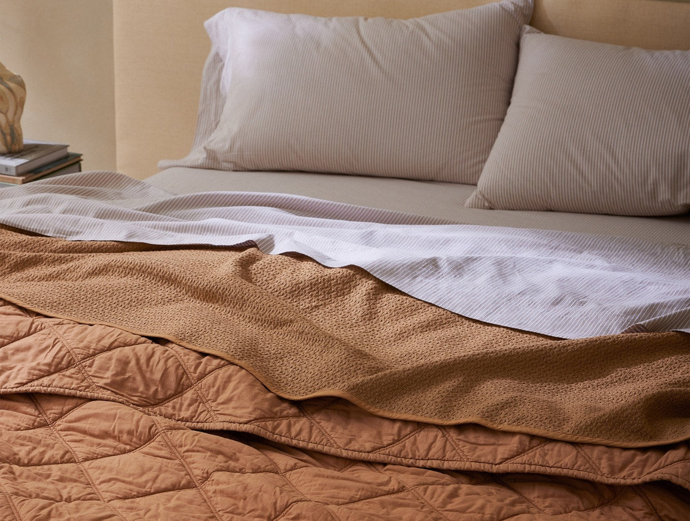 Coyuchi Honeycomb blanket in terracotta, draped across foot of bed showing quilted texture.